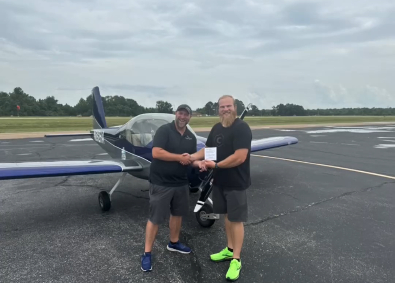 Adult pilot celebrating a certificate with his instructor beside a training aircraft